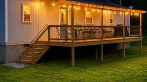 Een houten terras met buitenmeubilair, een trap en lichtjes.