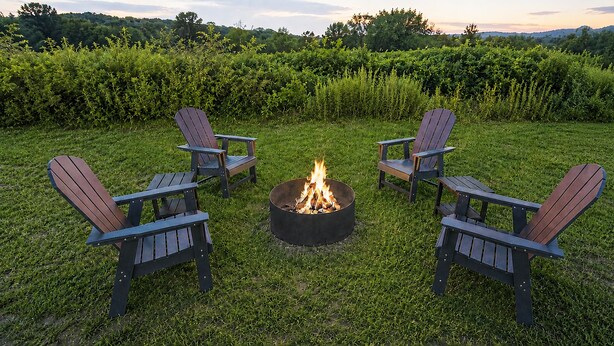 Een vuurkorf met vier Adirondack-stoelen eromheen, in een gazon.