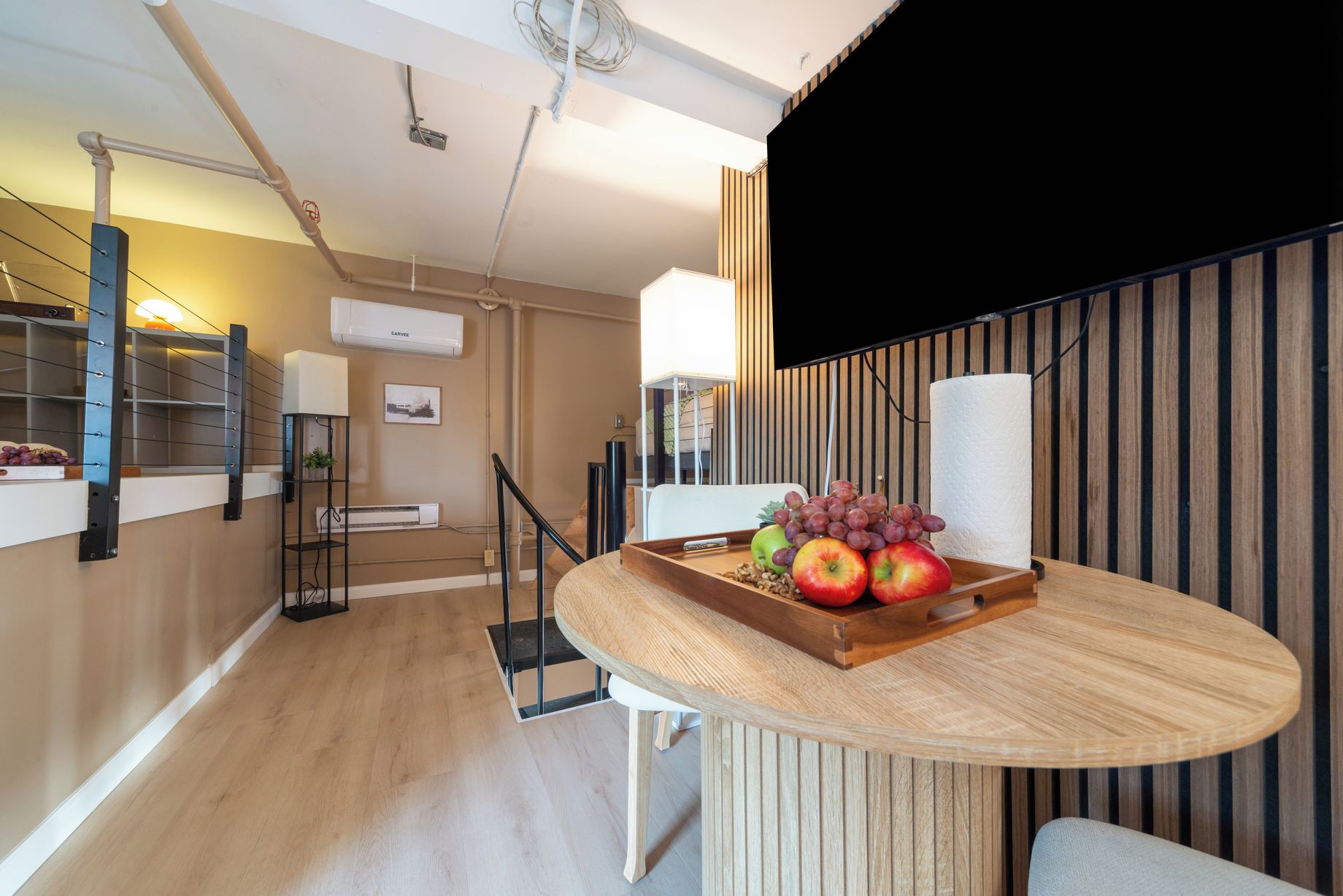 A modern kitchen with a wooden countertop, a fruit tray, and a dining area with a chair.