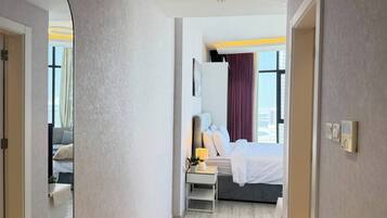 A hotel room with a bed, bedside table, lamp, and a view of the cityscape through large windows.