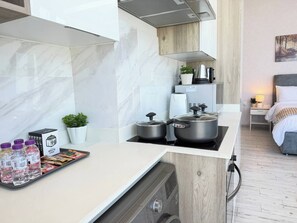 Cozinha compacta com fogão, panelas, geladeira pequena e bancada com água engarrafada e lanches.
