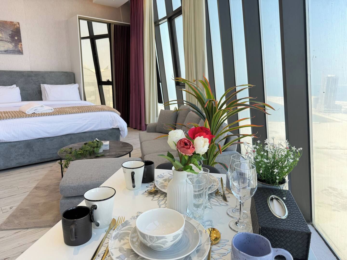 A hotel room with a bed, a sofa, a dining table set with plates, glasses, and a vase of flowers.