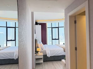 Et hotelværelse med to senge, et skrivebord med lampe og udsigt til høje bygninger.
