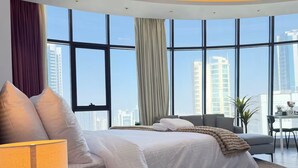 A modern hotel room with a large bed, a desk, and a view of the cityscape through floor-to-ceiling windows. - High-Floor Sea View Studio - Seef Area F296O (Seef)