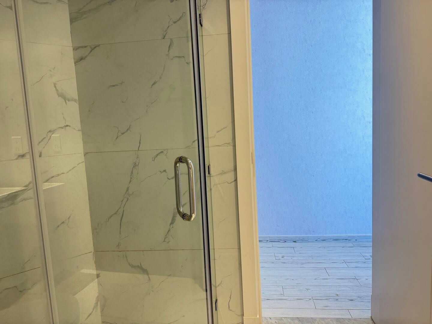 Une salle de bain avec un mur en marbre et une porte en verre donnant sur un balcon avec vue sur la mer.