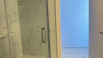 Une salle de bain avec un mur en marbre et une porte en verre donnant sur un balcon avec vue sur la mer.