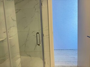 A bathroom with a marble wall and a glass door leading to a balcony with a view of the sea.