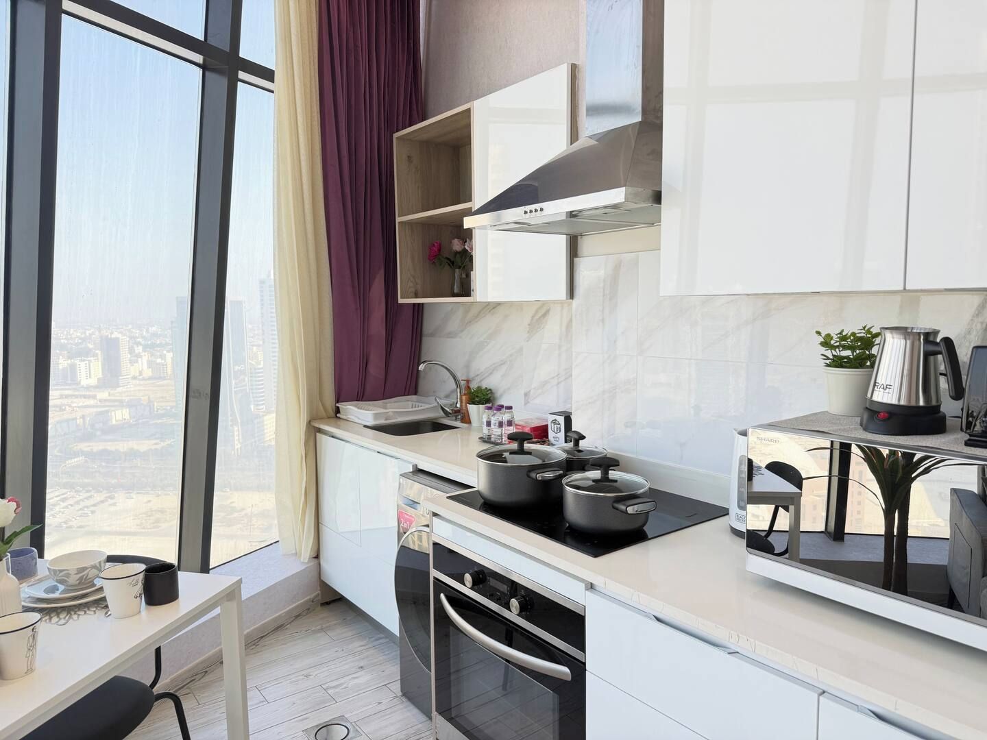 A modern kitchen with a large window, a stove, a sink, and a countertop with various items.