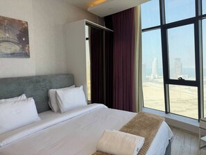 A hotel room with a large bed, a wardrobe, a view of the cityscape, and a painting on the wall.