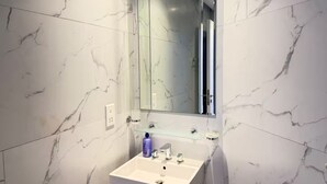 A bathroom with a white marble wall, a rectangular mirror, a white sink, and a glass shelf with a bottle. - High-Floor Sea View Studio - Seef Area F296O (Seef)