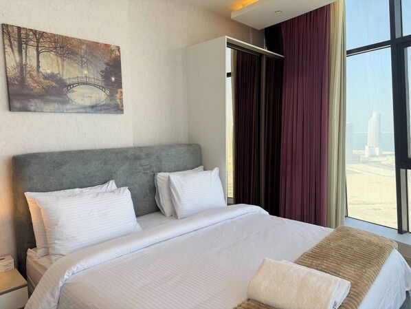 A hotel room with a large bed, a headboard, a painting on the wall, and a view of the city through the window.
