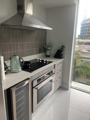 A modern kitchen with stainless steel appliances, a kettle, and a window with a view of a construction site. -  Luxury Designer-Furnished 2BR with 2 Large Terraces in Bay Harbor (Bay Harbor Islands)