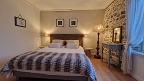Ein Schlafzimmer mit einem Bett, Nachttischlampen, einem Beistelltisch, einer Steinwand und einem Spiegel.