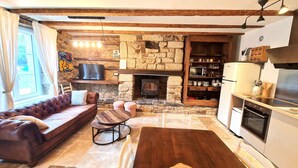 Ein gemütliches Wohnzimmer mit Kamin, einer Couch, einem Fernseher und einer Küchenzeile inklusive Kühlschrank und Backofen.