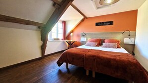 Ein Schlafzimmer mit geneigter Decke, einem Bett mit brauner Bettdecke, einem Nachttisch mit Lampe und einem Schild an der Wand.