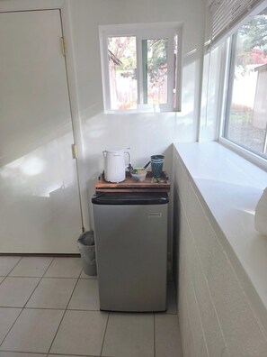 Eine kleine Küche mit einem Kühlschrank, einem Fenster und einer Arbeitsplatte mit Wasserkocher und Tasse.