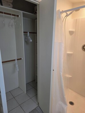 Ein Badezimmer mit Dusche, Toilette und Waschbecken. Ein Handtuchhalter und eine Tür zu einem Schrank sind vorhanden.