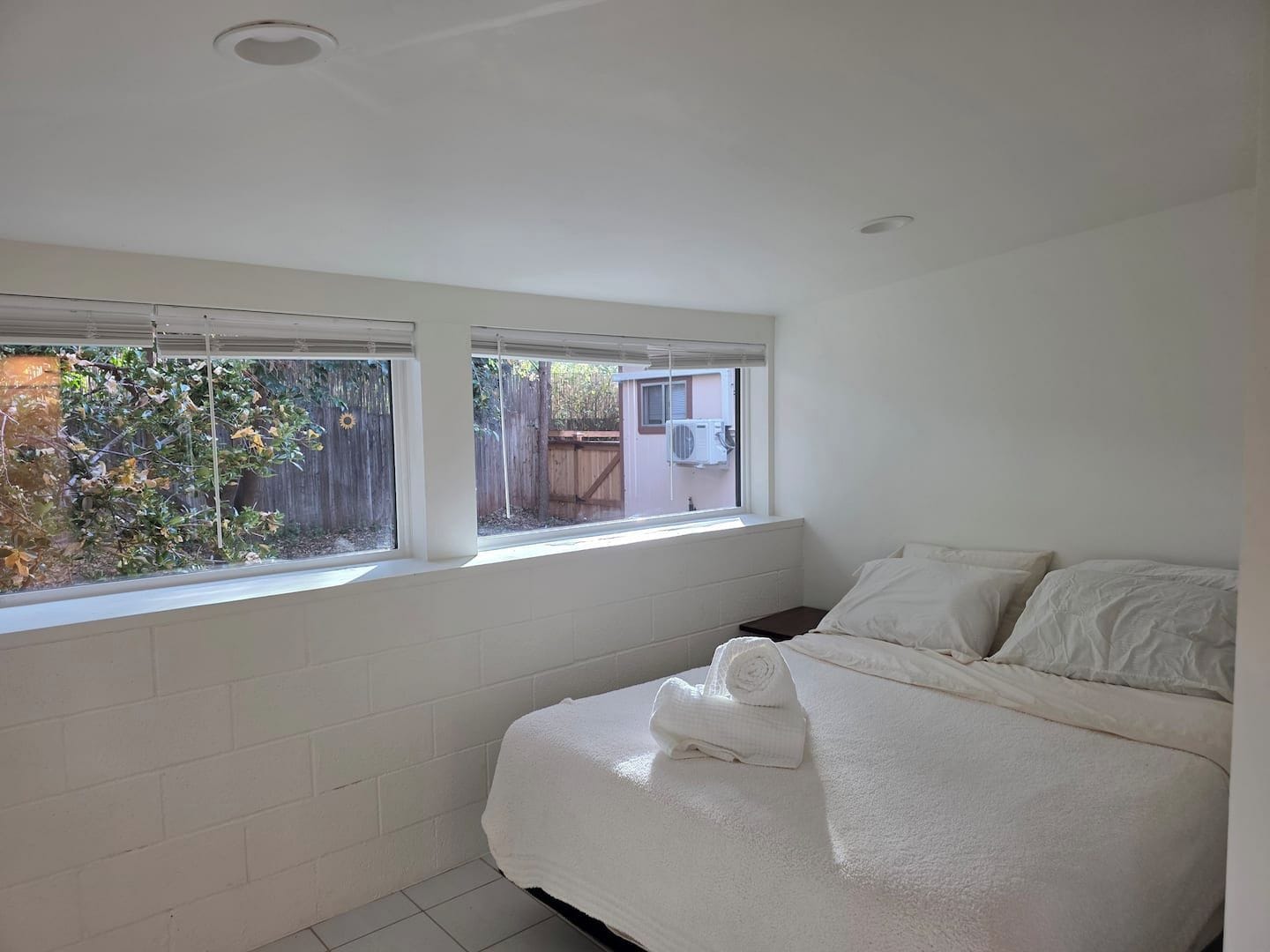 A bedroom with a bed, two windows, and a view of the outside.