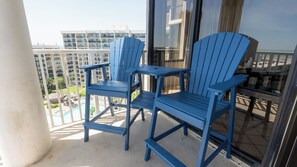 Een balkon met twee blauwe stoelen en een klein tafeltje, met uitzicht op een zwembad en gebouwen.