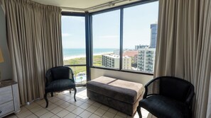 A room with a large window, two chairs, a small ottoman, and a dresser. - Saida Royale, Beachfront 10th Floor, 2BR, 3 Pools (South Padre Island)