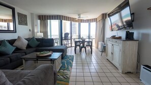 A living room with a sofa, coffee table, and a dining area with chairs and a table. - Saida Royale, Beachfront 10th Floor, 2BR, 3 Pools (South Padre Island)