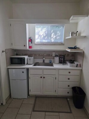 Una cocina compacta equipada con microondas, tostadora, lavamanos y un refrigerador pequeño.