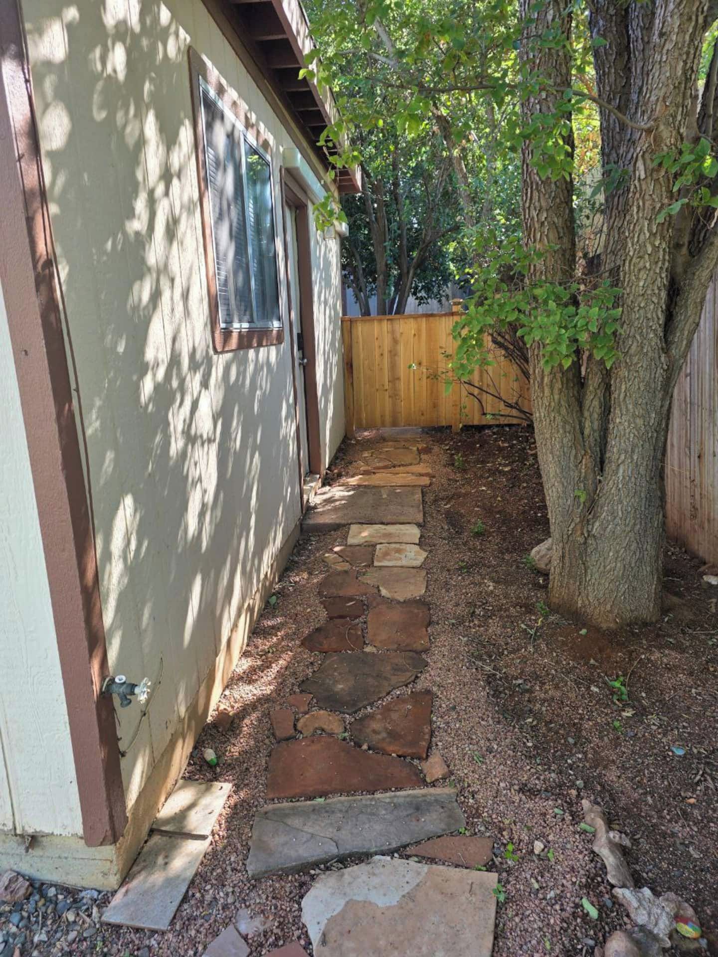 A stone pathway leading to a house with a wooden fence and a tree.