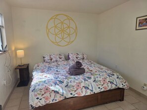 Un dormitorio con colcha estampada, cama de madera, lámpara de pared y decoración geométrica en la pared.