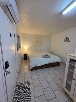 Un dormitorio con cama, lámpara de noche, equipo de aire acondicionado y un adorno geométrico en la pared.