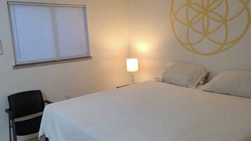 A bedroom with a bed, a chair, a lamp, and a window with blinds.