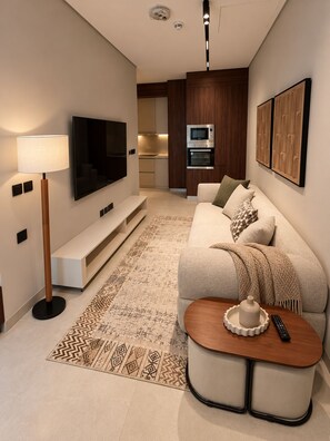 Ein modernes Wohnzimmer mit einer Couch, einem Couchtisch, einem Fernseher und einer Küchenzeile im Hintergrund.