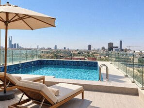 A rooftop swimming pool with lounge chairs and an umbrella, overlooking a cityscape. - LIV by Yamama - Park 91 (Riyadh)