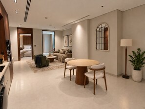 A modern hotel room with a dining area, a sofa set, a large window with a view, and a potted plant. - LIV by Yamama - Park 91 (Riyadh)