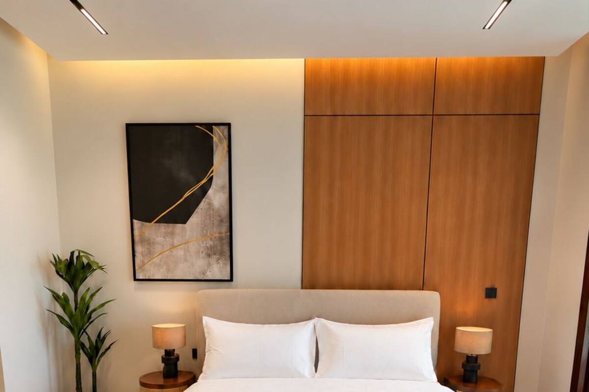 A modern bedroom with a large bed, two bedside tables, a wall-mounted light, and a potted plant.