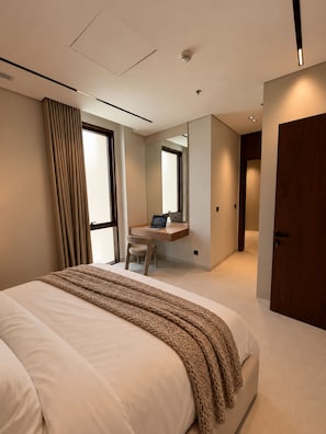 A modern hotel room with a large bed, a desk with a laptop, a mirror, and a door. - LIV by Yamama - Park 91 (Riyadh)