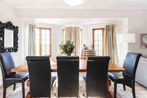 Un comedor con una mesa de madera y sillas negras, un espejo en la pared y un jarrón con flores sobre la mesa.