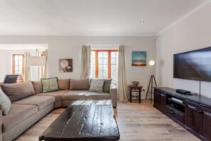 A living room with a sectional sofa, a coffee table, a TV, and a lamp. - Spacious 4-bedroom house in amazing Cape Town with AC (Cape Town)