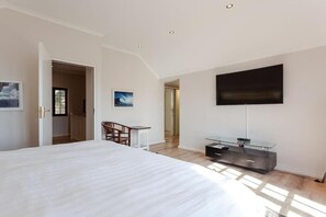 A bedroom with a large bed, a desk, a chair, a flat-screen TV, and a glass cabinet. - Spacious 4-bedroom house in amazing Cape Town with AC (Cape Town)