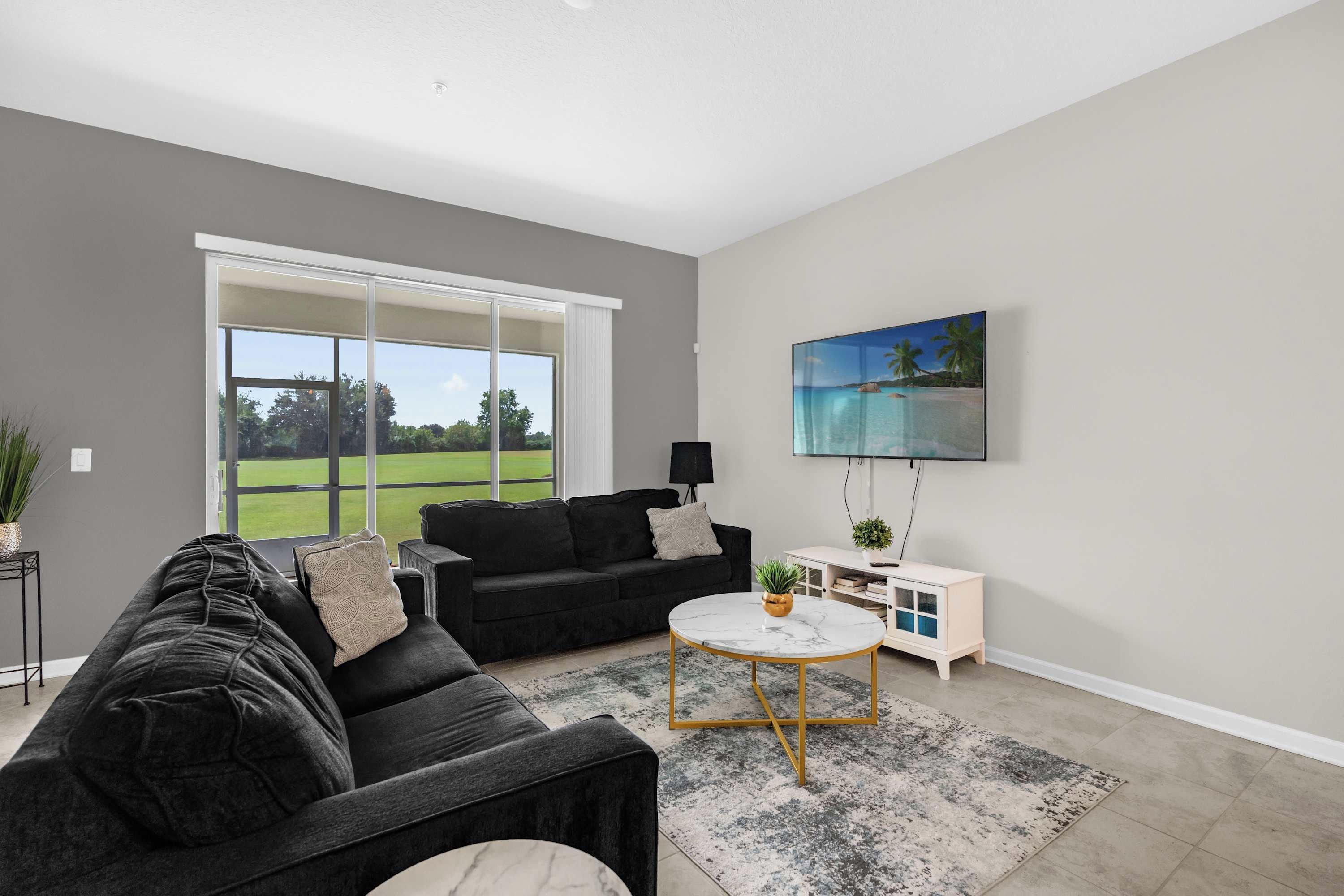 A modern living room with a black sofa, a round coffee table, and a TV mounted on the wall.
