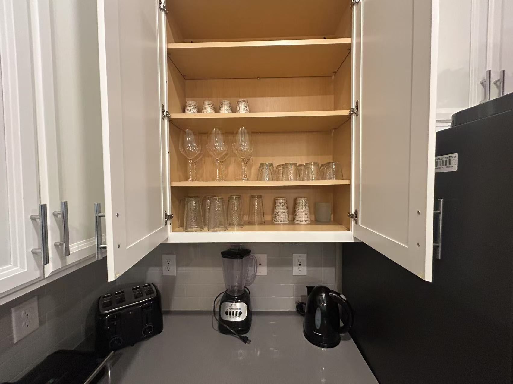 Uma cozinha com armário embutido contendo copos de vinho e potes, uma torradeira, um liquidificador e uma chaleira.