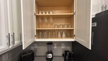 Uma cozinha com armário embutido contendo copos de vinho e potes, uma torradeira, um liquidificador e uma chaleira.