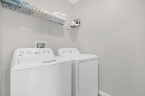 Una sala de bugaderia amb dues rentadores blanques, un escurabutaps i una petita estant amb tovalloles i una fotografia emmarcada.