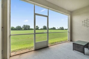 Ein Zimmer mit großem Fenster, einem Korbstuhl und einem Betonboden.