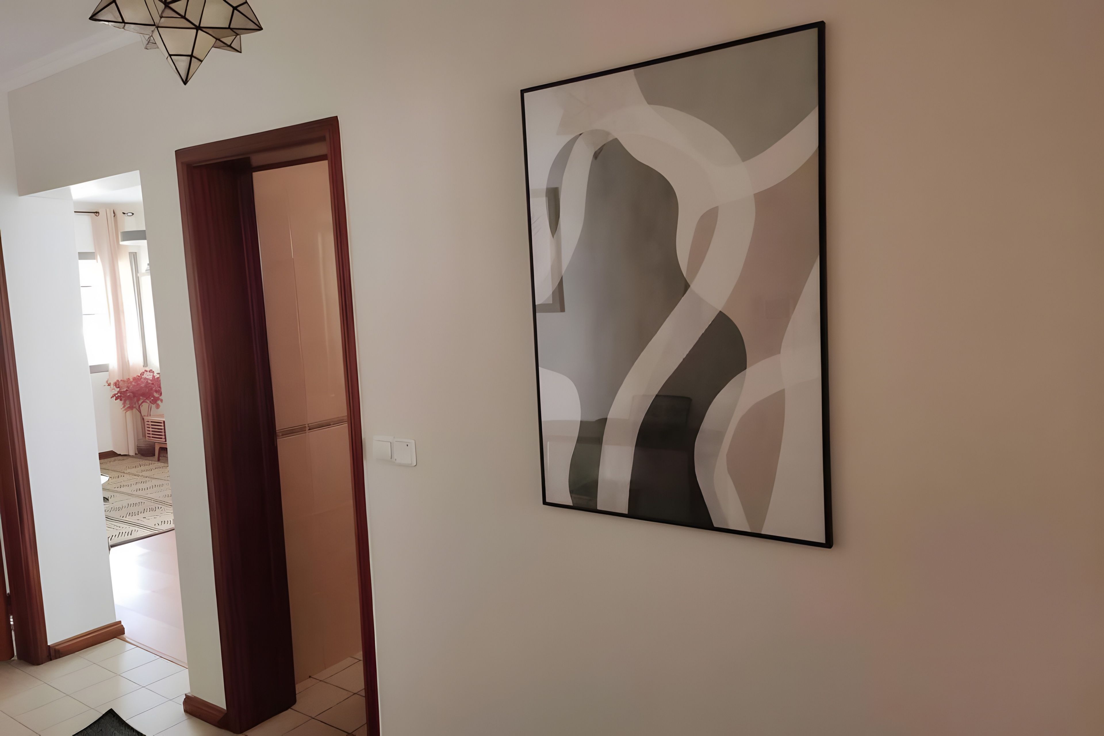 Um corredor com uma obra de arte abstrata emoldurada na parede, uma porta de madeira e piso de azulejos.