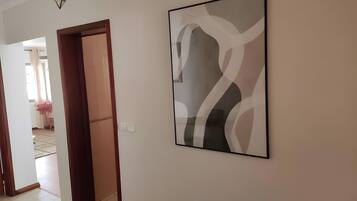 Um corredor com uma obra de arte abstrata emoldurada na parede, uma porta de madeira e piso de azulejos.