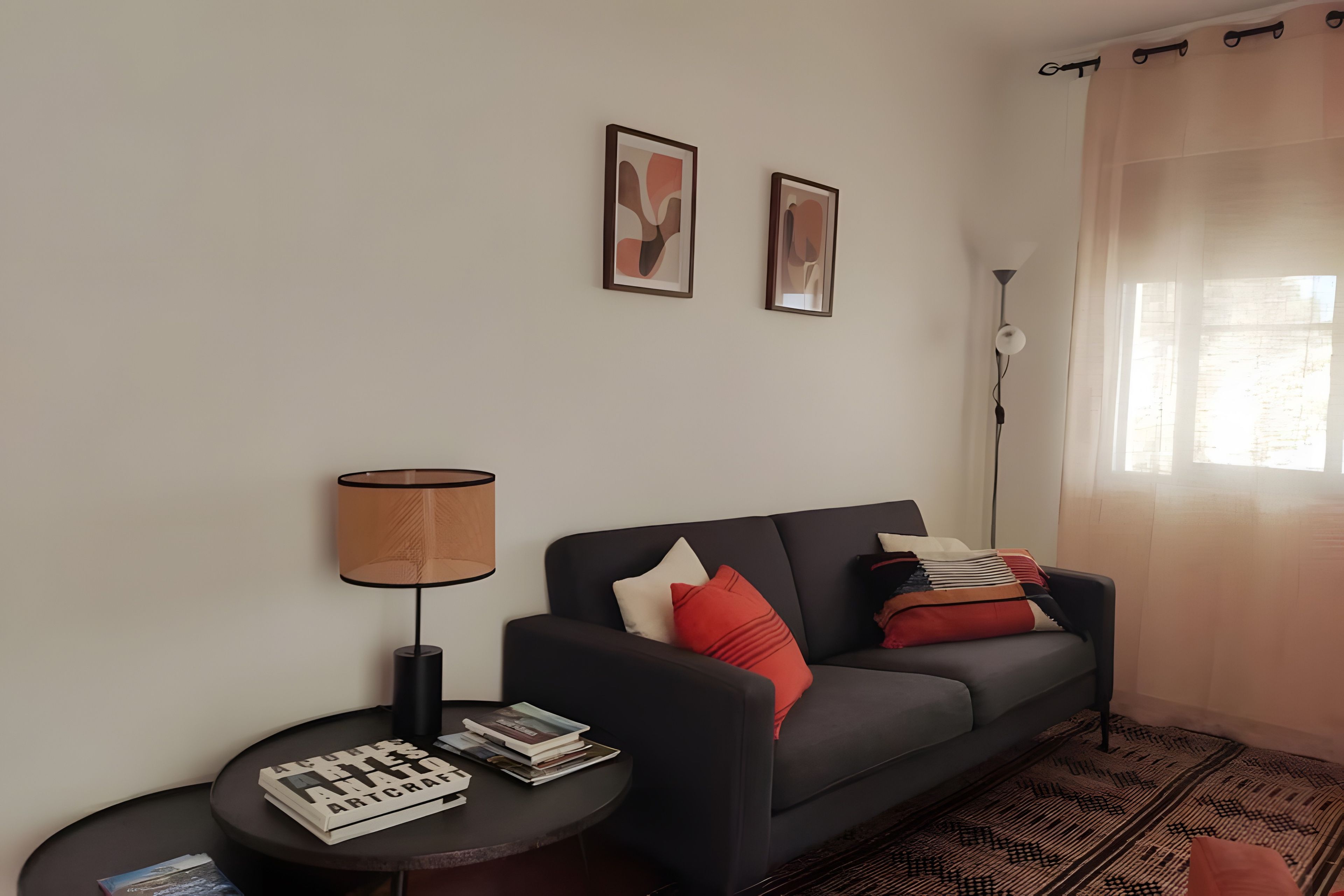 Una sala de estar con un sofá, una mesita de noche con una lámpara y dos cuadros en la pared.