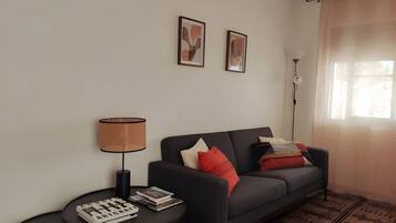 Una sala de estar con un sofá, una mesita de noche con una lámpara y dos cuadros en la pared.