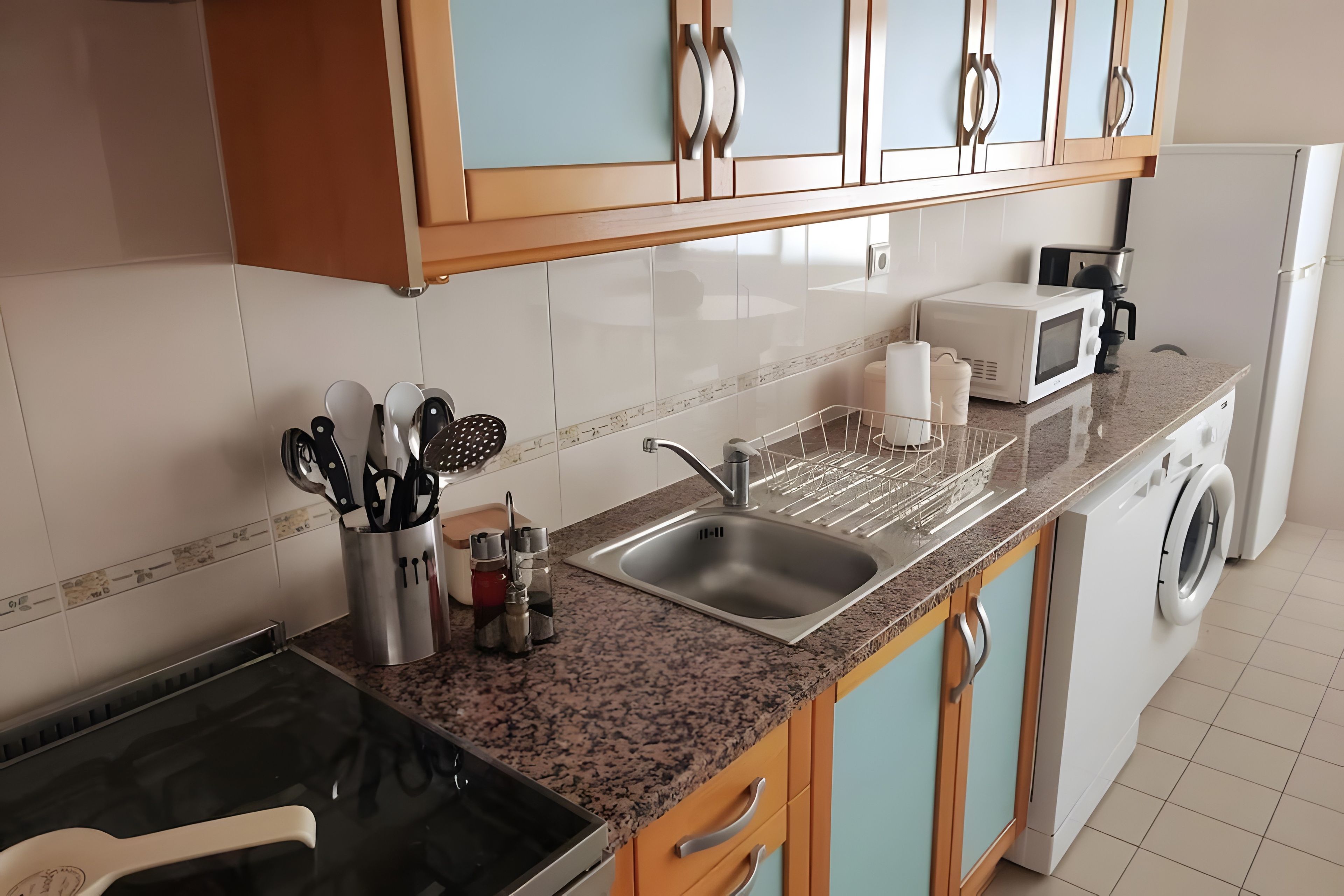 Cozinha moderna com bancada de granito, pia de aço inoxidável e máquina de lavar embutida.
