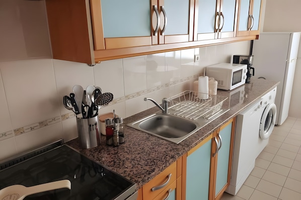Cozinha moderna com bancada de granito, pia de aço inoxidável e máquina de lavar embutida.