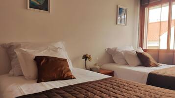 Habitación de hotel con dos camas, cada una con ropa de cama blanca y almohadas marrones. Se ve una ventana al lado derecho, y hay obras de arte en las paredes.